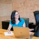 wo people smiling and talking to each other at a table with a laptop discussing the velocity of sales.